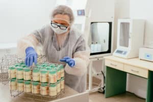 Healthcare worker in sterile uniform sorts labeled breast milk bottles in wire rack. Process of safe storage preparation for neonatal or donor milk use.